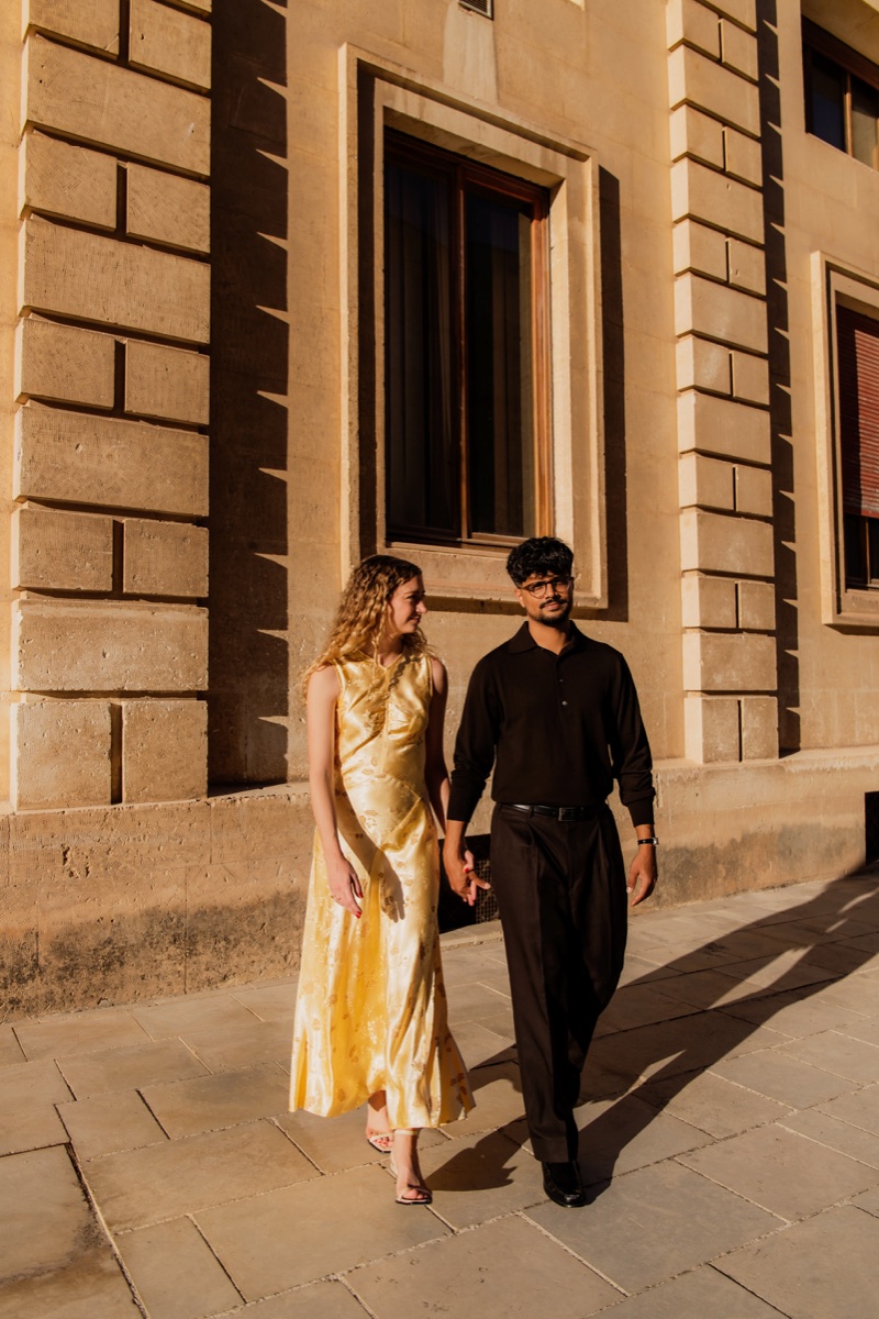 Madeline and Rondeep walking hand in hand past a sandstone building